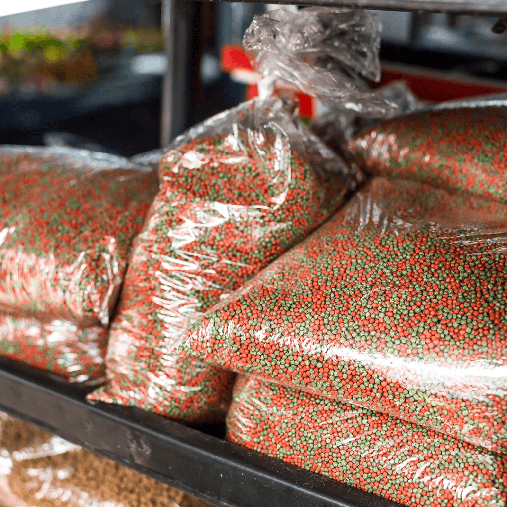 Clear plastic bags filled with small red and green pellets are stacked on a shelf, likely for sale at a market or store—perfect for aquarium maintenance and avoiding common fish tank cleaning mistakes.